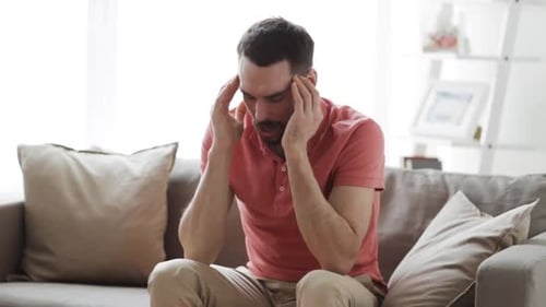 Man on Couch Massaging Temples with Headache
