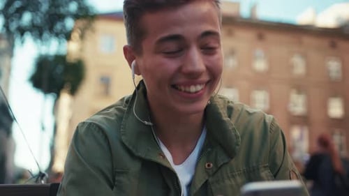Close Up Face Handsome Young Man Use Phone Listen Music in Headphone Look Around Sitting on Street