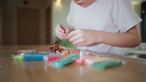 Boy in White Shirt Sitting at Wooden Table Creating Colorful Plasticine Figures