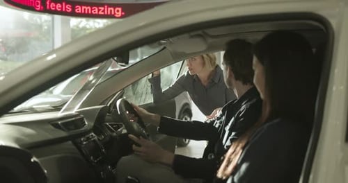 Sales woman advising couple sitting in new electric car in automotive showroom
