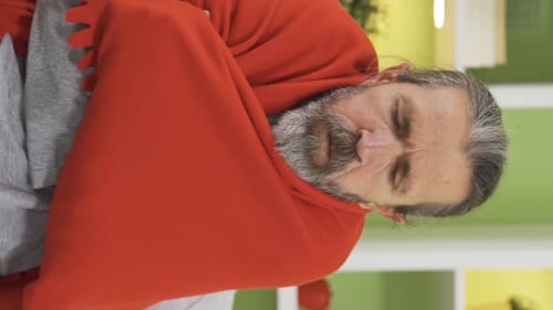 Vertical Video of Sick old man with health problems is cold at home and hugging a blanket.