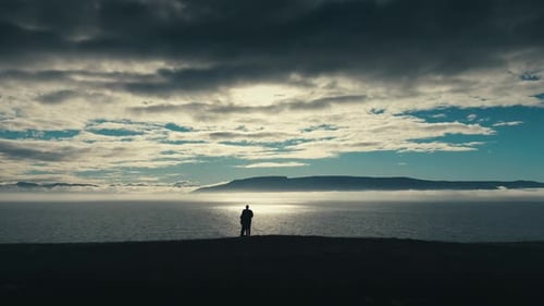 Epic and romantic aerial drone shot of couple looking out over incredible ocean sunset. The camera f