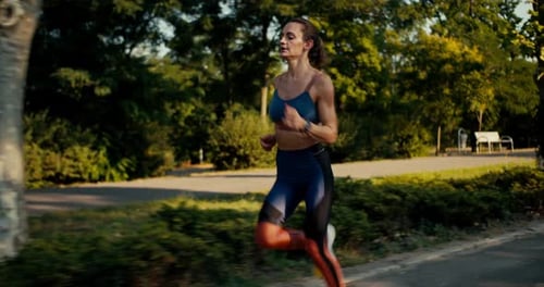 A Sports Girl in a Sports Summer Uniform Runs at Speed in the Morning Park Fitness and Jogging to