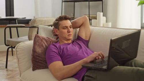 Caucasian Man Works at a Computer on a Sofa