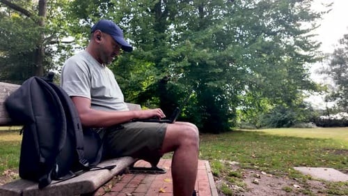 South Asian man remote working on park bench