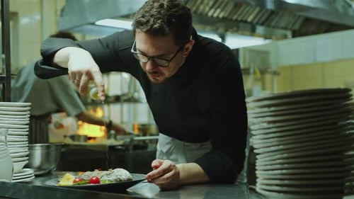 Chef Adding Olive Oil to Fish Served on Plate in Restaurant Kitchen