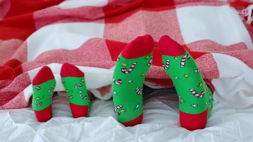 Children's and adult feet in bright colorful green Christmas socks are visible from under the plaid