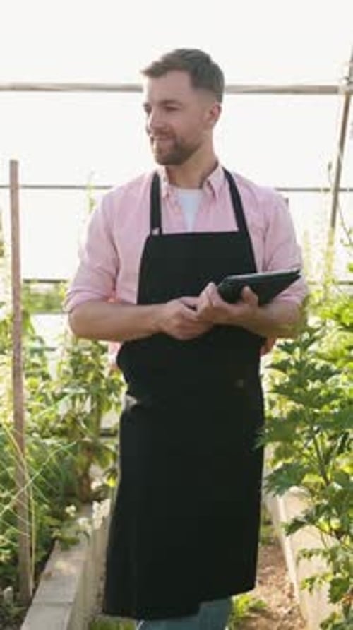 Man Walks Through Greenhouse with Tablet