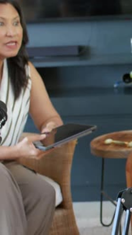 Vertical video: Tapping tablet, woman in striped top speaking into boom mic in studio for podcast