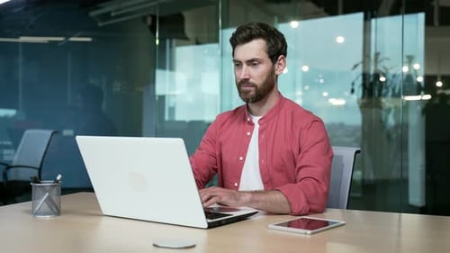 Handsome bearded employee businessman worker works on laptop in modern glass office. confident male