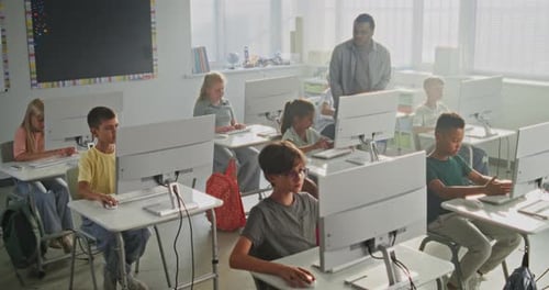 Estudiantes de primaria que trabajan en proyectos creativos sobre computadoras Un profesor guía a diversos niños
