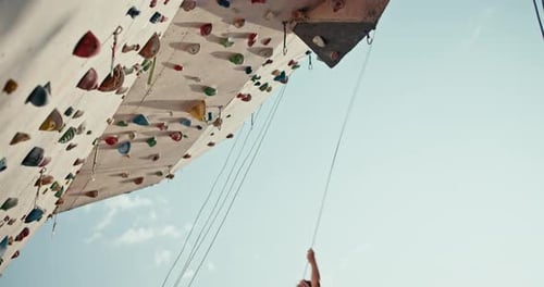 Vue du bas : une fille athlétique grimpe à la hauteur requise sur un mur d'escalade puis descend