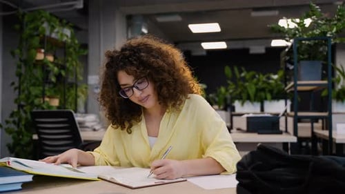 Focused University Student Writing Notes in Modern Library