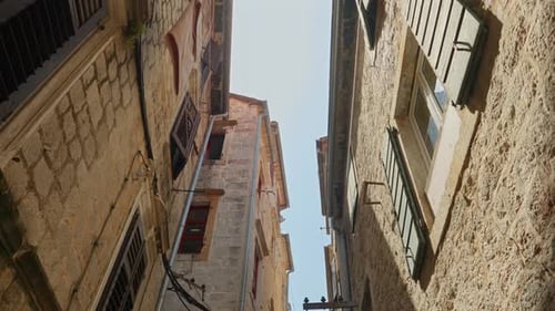 Walking on old town narrow street and looking up at the tiled roof and stone walls