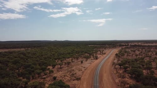 Drone flying over a very remote country road surrounded with red soil and trees in the Australian ou