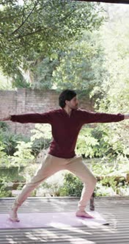 Vertical video of biracial man practicing yoga on sunny terrace, slow motion