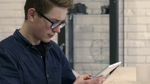 Teenager Uses Tablet Sitting at Table Indoors
