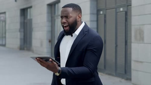 Shocked african american businessman looks at tablet on city street in slow motion