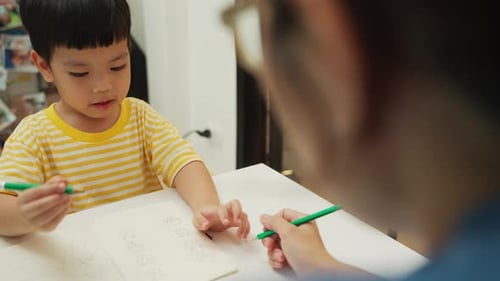 Asiatische Mutter hilft ihrem kleinen Jungen während der Homeschool-Zeit zu Hause zu lernen