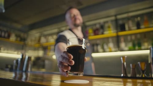 The Bartender Puts a Glass of Dark Beer on the Counter