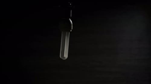 Une lampe fluorescente en spirale scintille, s'allume et se balance sur un fil électrique