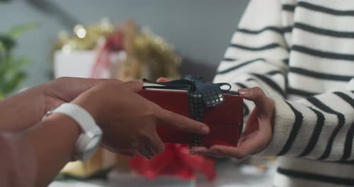Close up of girl hands giving present gift box winter christmas decorations on table.