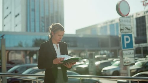 Bank Manager Reviewing Documents Outside Urban Office in Bright Sunlight