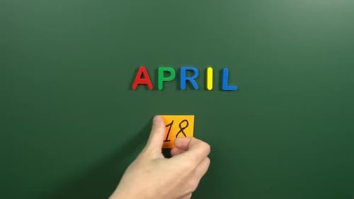 Hand sticking a sticker 18 April calendar day on school board. 18 date of April. Eighteenth day