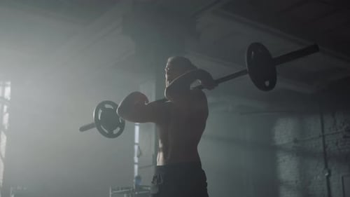 Shirtless bodybuilder performing front squats with barbell during fitness workout