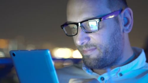 Young man enjoys nighttime internet browsing on tablet at rooftop bar terrace