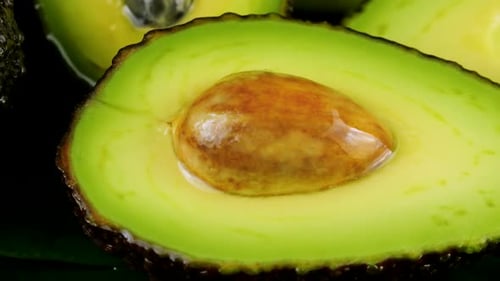 Drops of water fall on avocado fruits with leaves on a black background. Raw Fruits, healthy food.