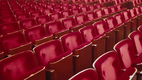 Wide shot passing by empty red audience seats in an empty public theatre