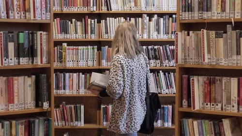 Young girl walking between bookshelves in library, static shot with books all around