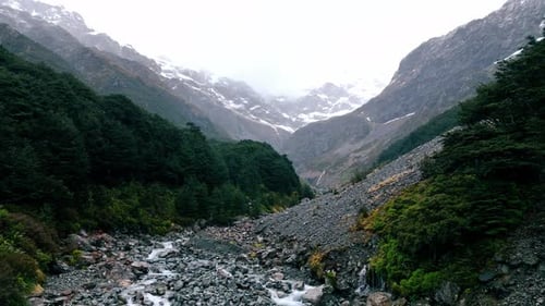 Aerial View of a River Cascading Through Rocky Terrain Into Lush Green Valleys Under a Cloudy Sky
