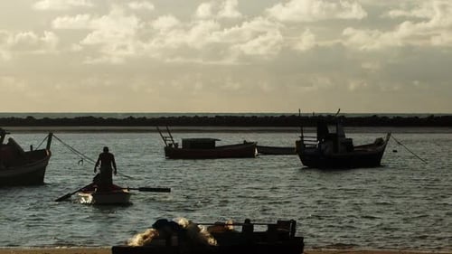 Silhouette zweier Männer auf einem Ruderboot in einer kleinen Bucht voller vor Anker liegender Boote in der goldenen Stunde. Sup