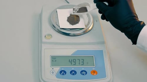Weighing Dark Powder on Digital Scale in Laboratory