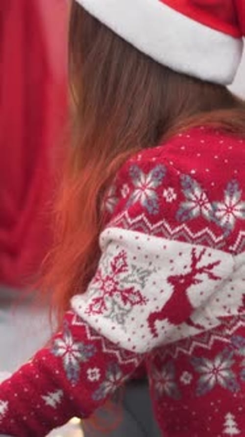 Girl Unwraps Christmas Gift by Christmas Tree