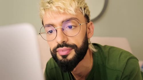 Close-up, young blond man with a beard uses a laptop while lying on the sofa in a cozy living room