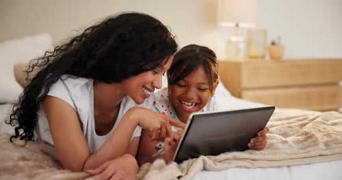 Mother and Daughter Laughing Together at Tablet on Bed