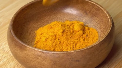 Spoon puts Turmeric Powder spice in wooden bowl on wooden board and rotate. Dry seasoning in spoon