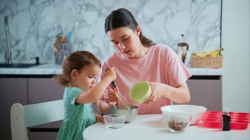 Girl mixes ingredients with adult in bright kitchen