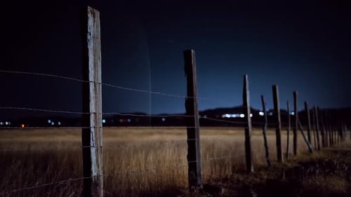 Rustic Barbed Wire Fence in Rural Field at Night with Distant City Lights