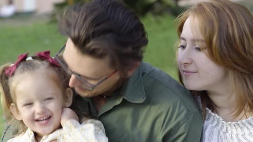 A happy young family, father and mother taking time with their cheerful daughter in the city park
