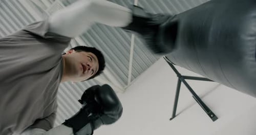 Slow Motion of Professional Male Boxer Exercising with Punching Bag in Sports Center Hitting