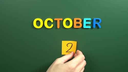 Hand sticking a sticker 2 October calendar day on school board. 2 date of October. Second day