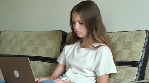 Teenager-Mädchen tippt auf der Laptop-Tastatur, während sie zu Hause auf dem Sofa sitzt