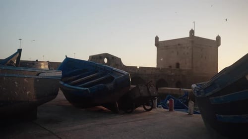 Essaouiras ikonische blaue Boote liegen am Hafen mit der Festung Skala im Hintergrund, wenn die Morgendämmerung aufgeht