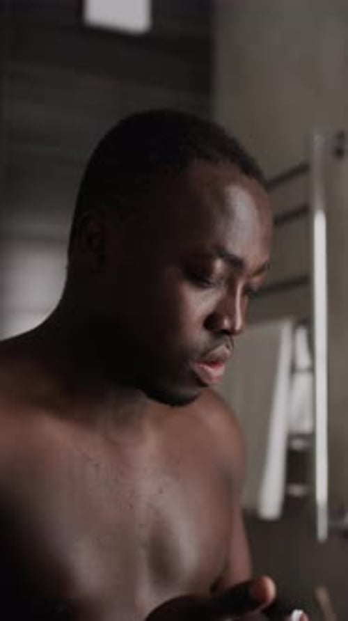 Man Massaging Skincare Product onto Face in Bathroom