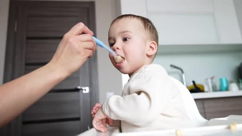 Adorable Infant Being Fed in Kitchen Highchair