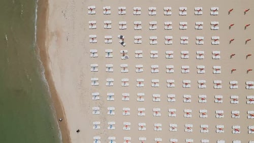 A Sandy Beach Stretches Along the Seaside Adorned with Empty Sun Loungers Aerial View